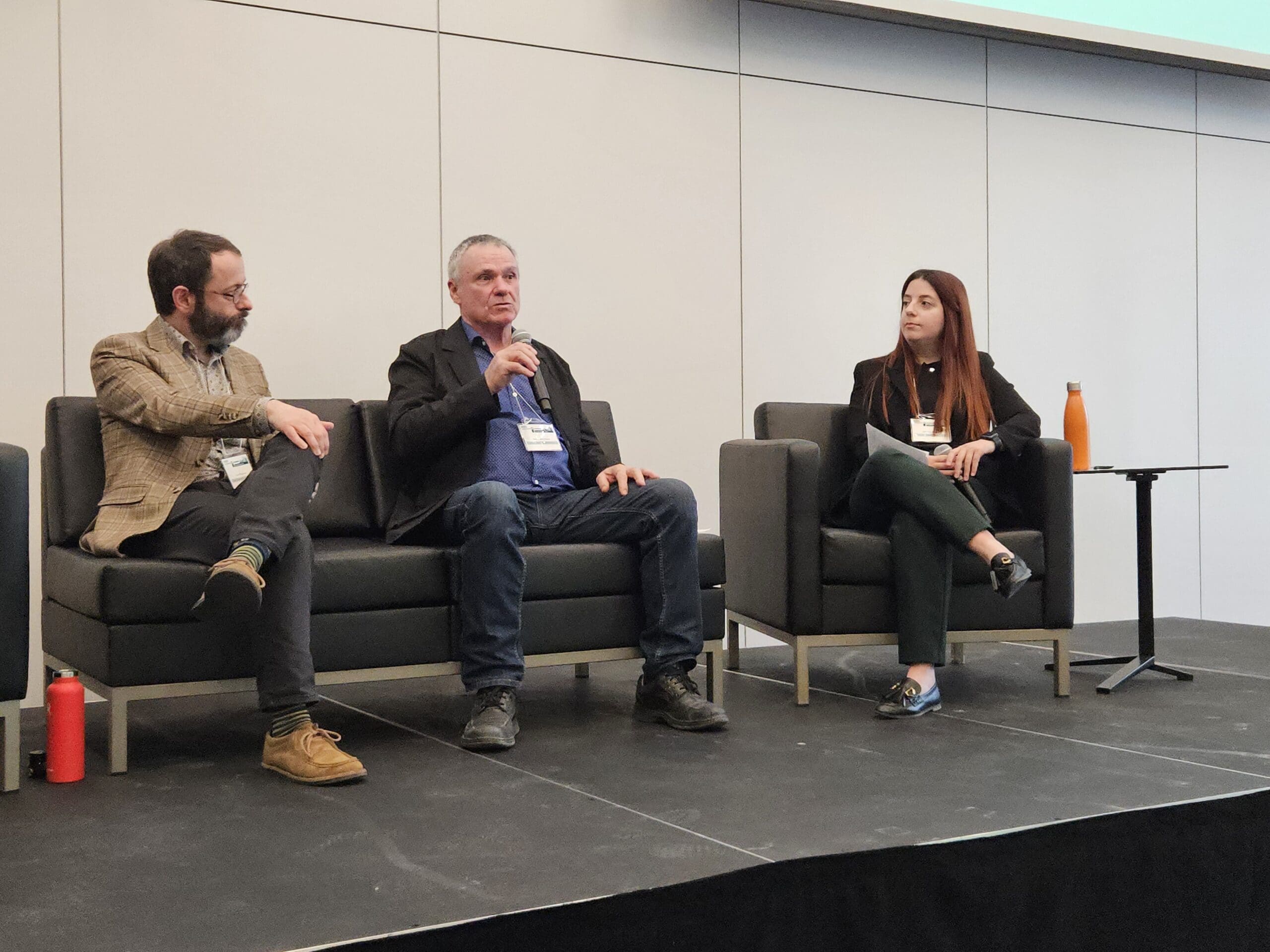 "Une personne se tient sur la scène et parle dans un microphone lors du symposium sur les bâtiments sans carbone. Derrière elle