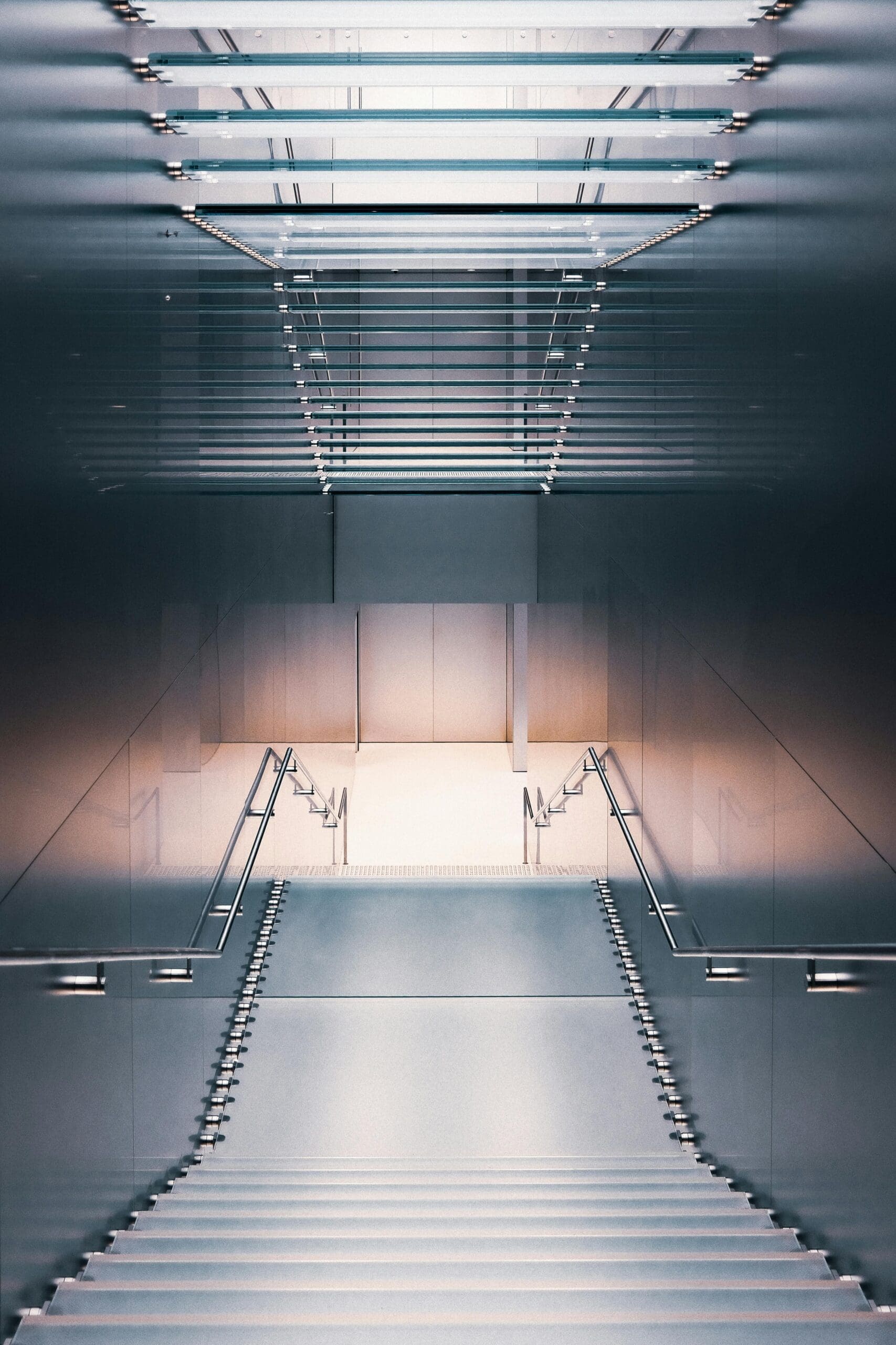 "Escalier moderne et élégant menant vers le bas dans un espace architectural minimaliste. Les marches sont flanquées de rampes métalliques et éclairées par un éclairage d'ambiance doux depuis le haut et le bas
