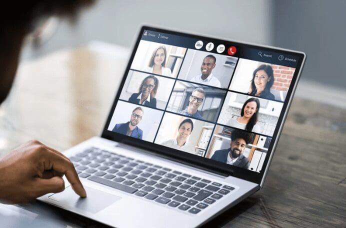 "Une personne participe à une vidéoconférence sur un ordinateur portable. L'écran affiche neuf personnes différentes dans des fenêtres de flux vidéo distinctes