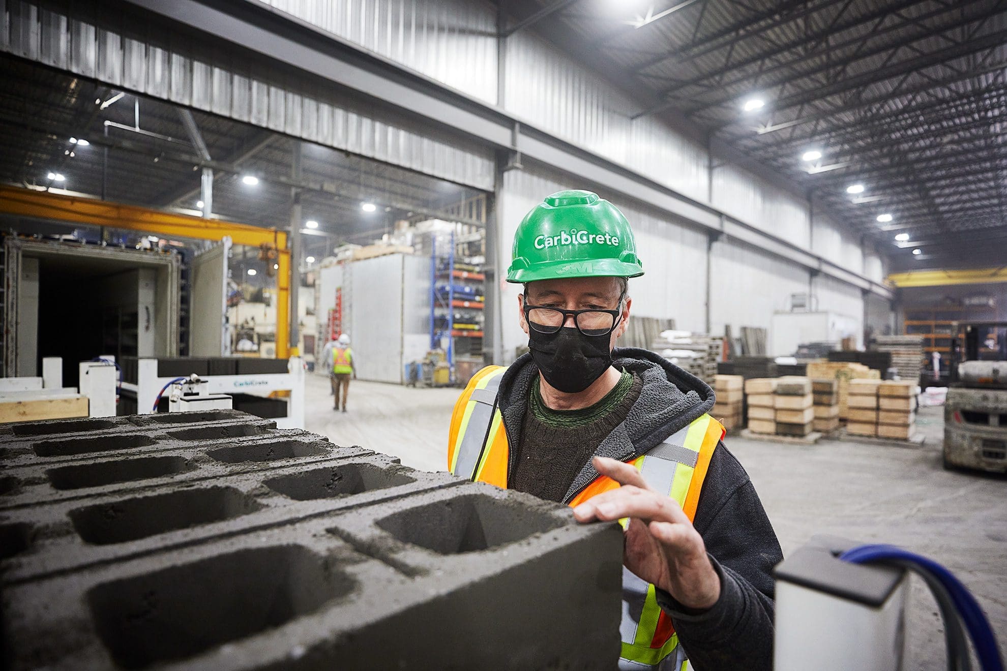 Un ouvrier de l'usine CarbiCrete-Pation portant un masque et un casque de protection, soucieux de la sécurité et de la productivité dans un environnement de production.