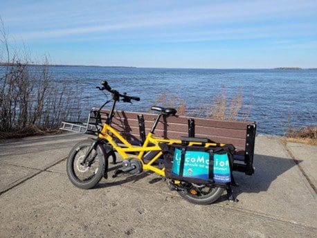 Vélo Locomotion avec un banc arrière pour embarquer une autre personne acoté sur un banc devant un plan d'eau 