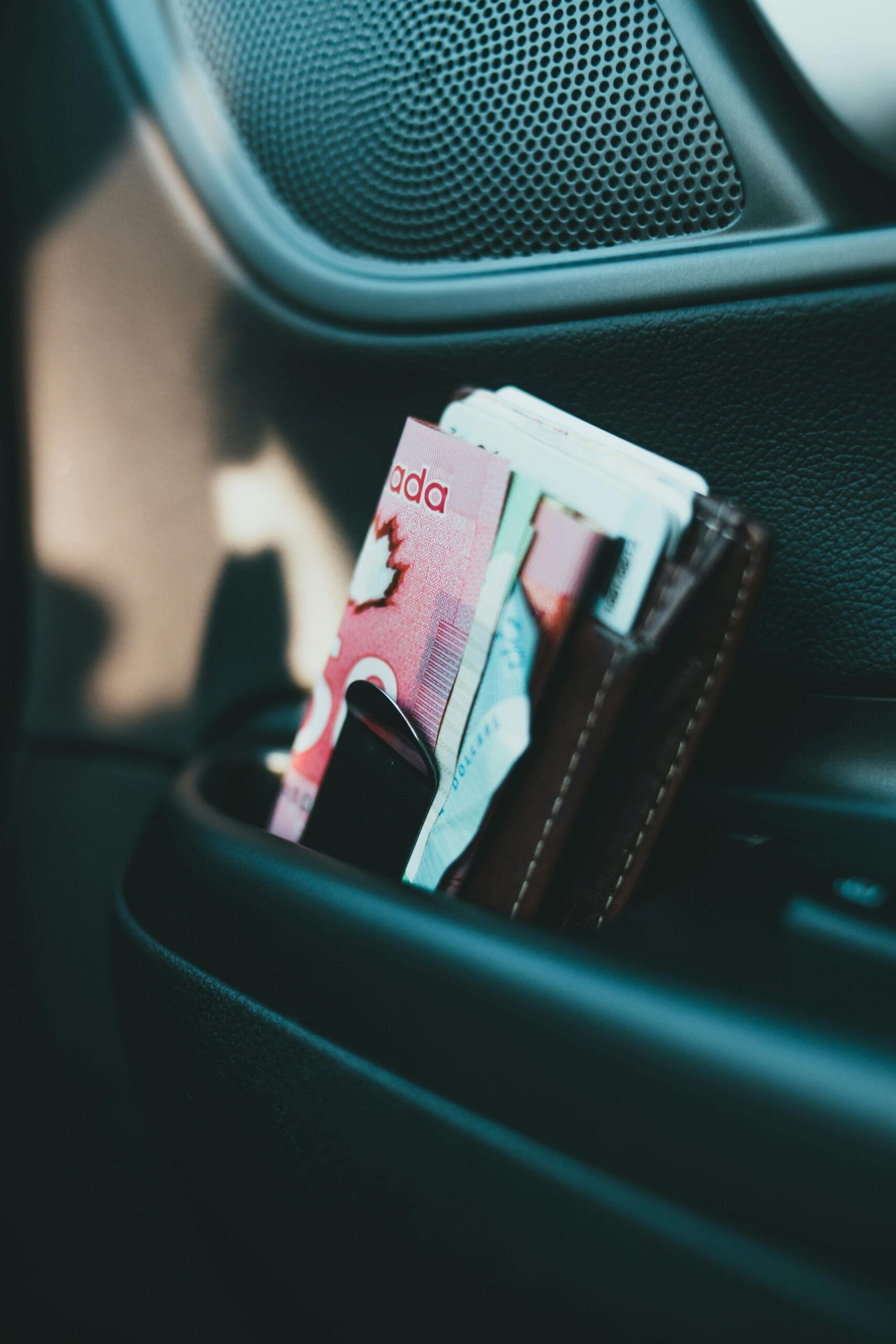 Un portefeuille rempli de billets de banque canadiens, dont une feuille d'érable visible, est placé à la verticale dans le compartiment latéral d'une portière de voiture.