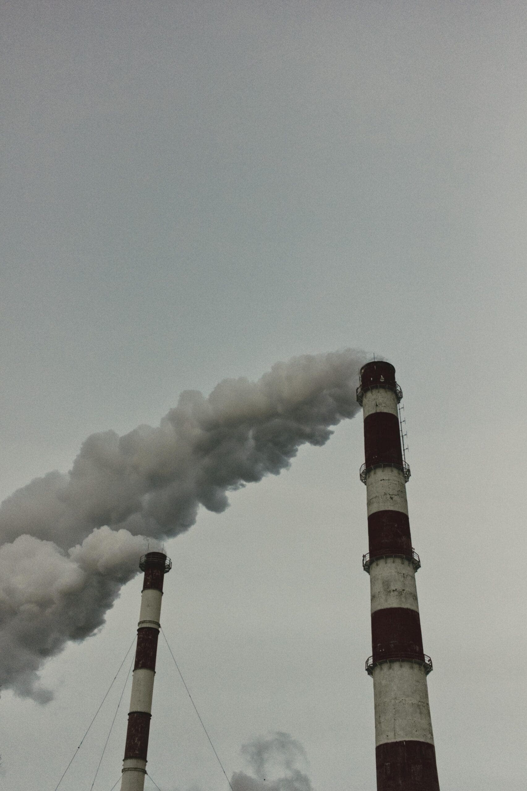 Deux cheminées industrielles sur fond de ciel gris émettent une fumée épaisse et sombre, soulignant l'atmosphère couverte et l'impact sur l'environnement.