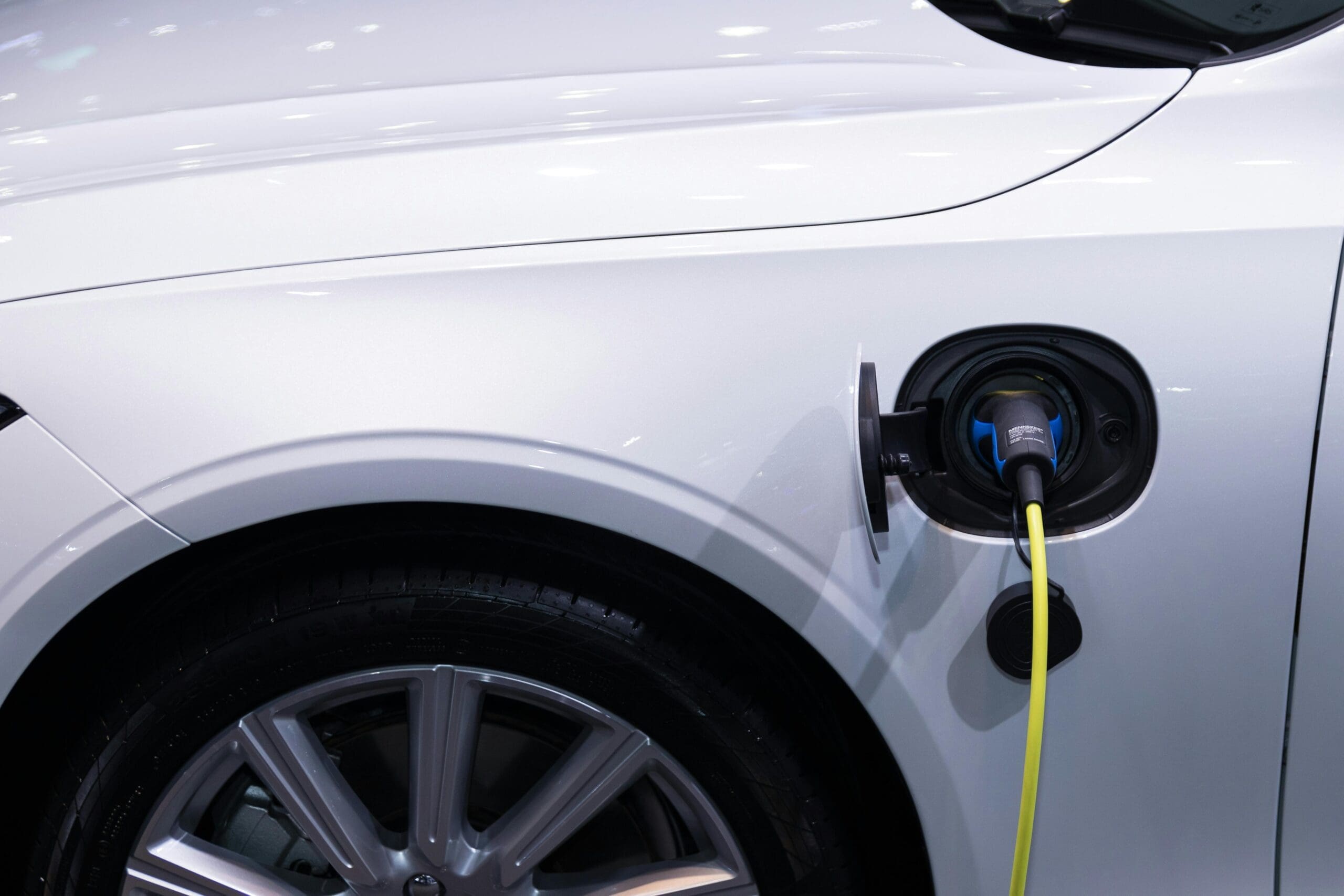 Gros plan sur une voiture électrique argentée dont le port de charge est ouvert. Un câble de recharge jaune est branché dans la prise circulaire. Une roue élégante et une partie de la carrosserie de la voiture sont visibles sur un arrière-plan flou.