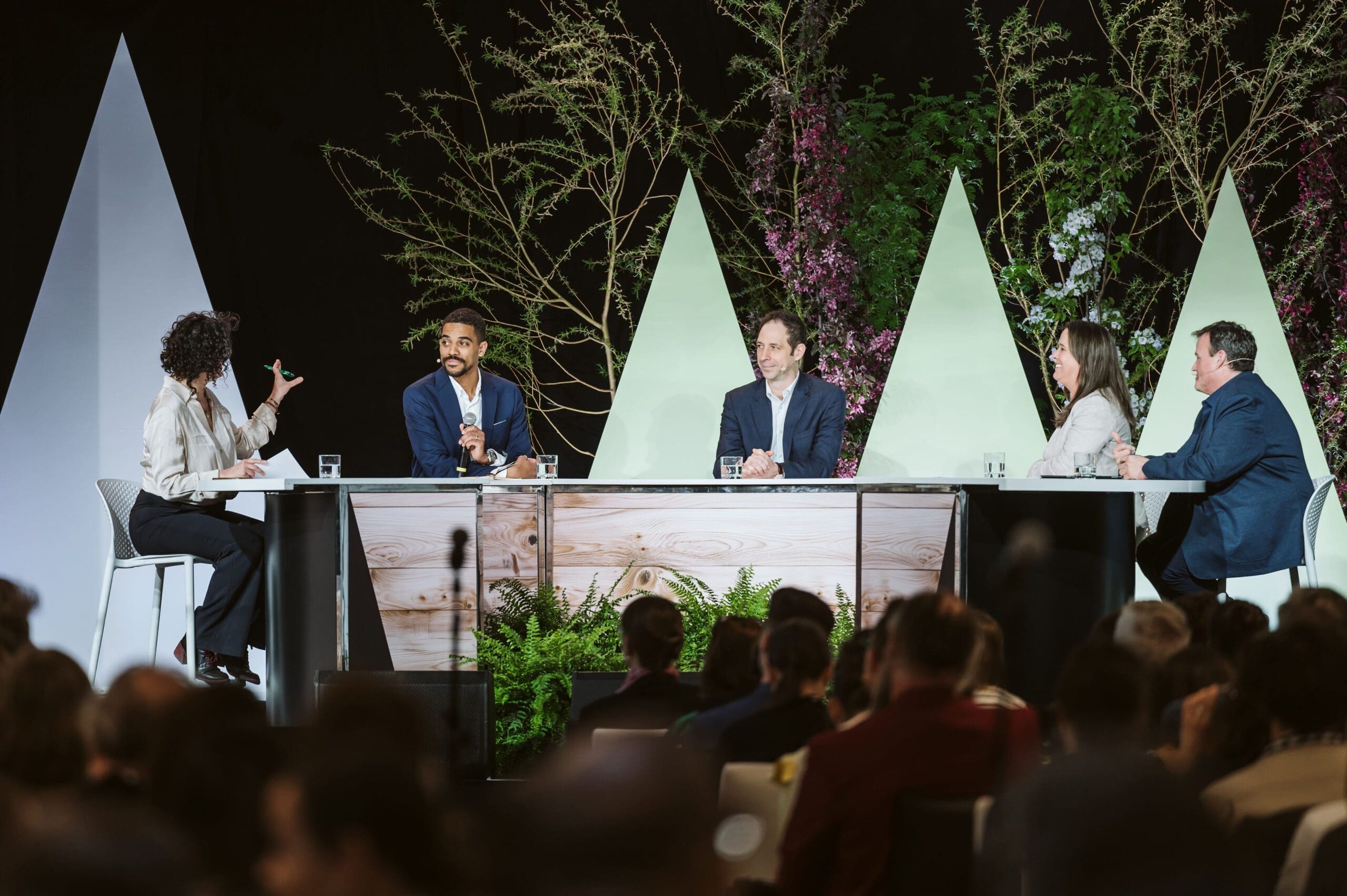 Un large public est assis en rangs face à une scène lors d'une conférence du Sommet Climat 2023. Sur la scène se trouvent un orateur sur un podium, plusieurs écrans et des bannières. La salle est bien éclairée par de grandes fenêtres et plusieurs écrans montrent l'orateur.