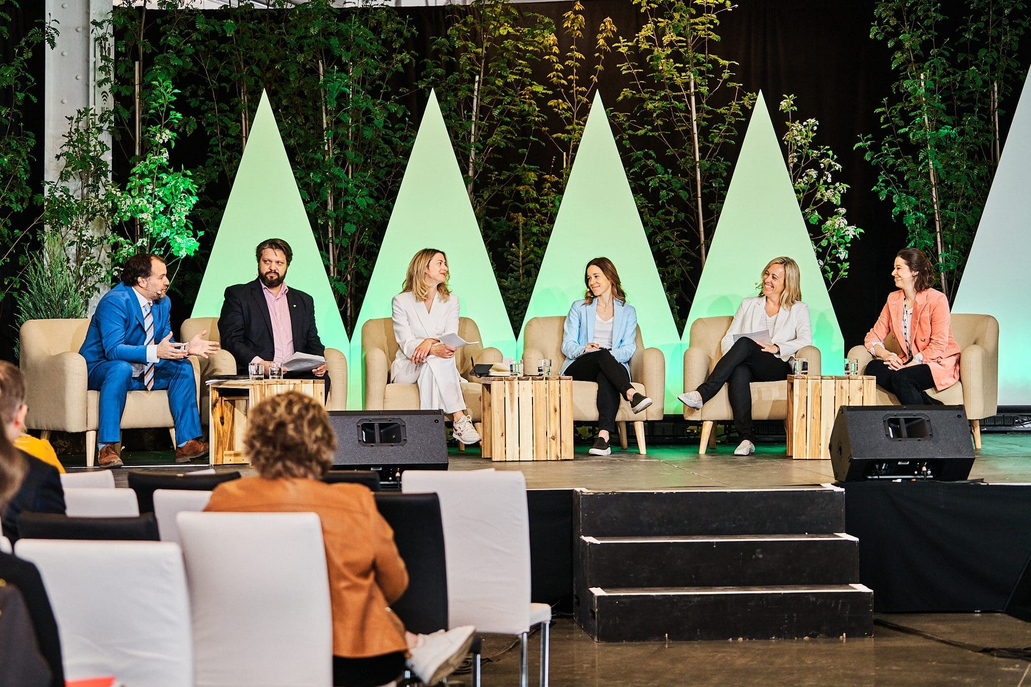 Un panel de six personnes est assis sur une scène pour le Sommet Climat 2023 avec une verdure triangulaire et une toile de fond sombre. Elles discutent, chacune assise sur un canapé ou une chaise. Le public observe la scène depuis des rangées de sièges au premier plan.