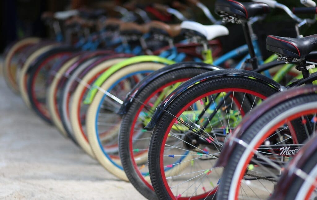 Une rangée de vélos colorés alignés sur un trottoir pavé. Les vélos sont équipés de gros pneus avec des jantes de différentes couleurs et sont garés les uns près des autres, créant un motif de roues qui s'étend au loin.