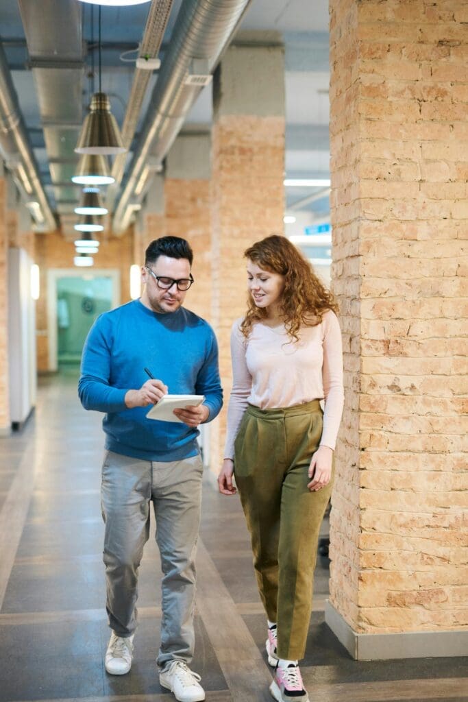 Un homme et une femme discutent en marchant dans un bâtiment. L'homme prend des notes.